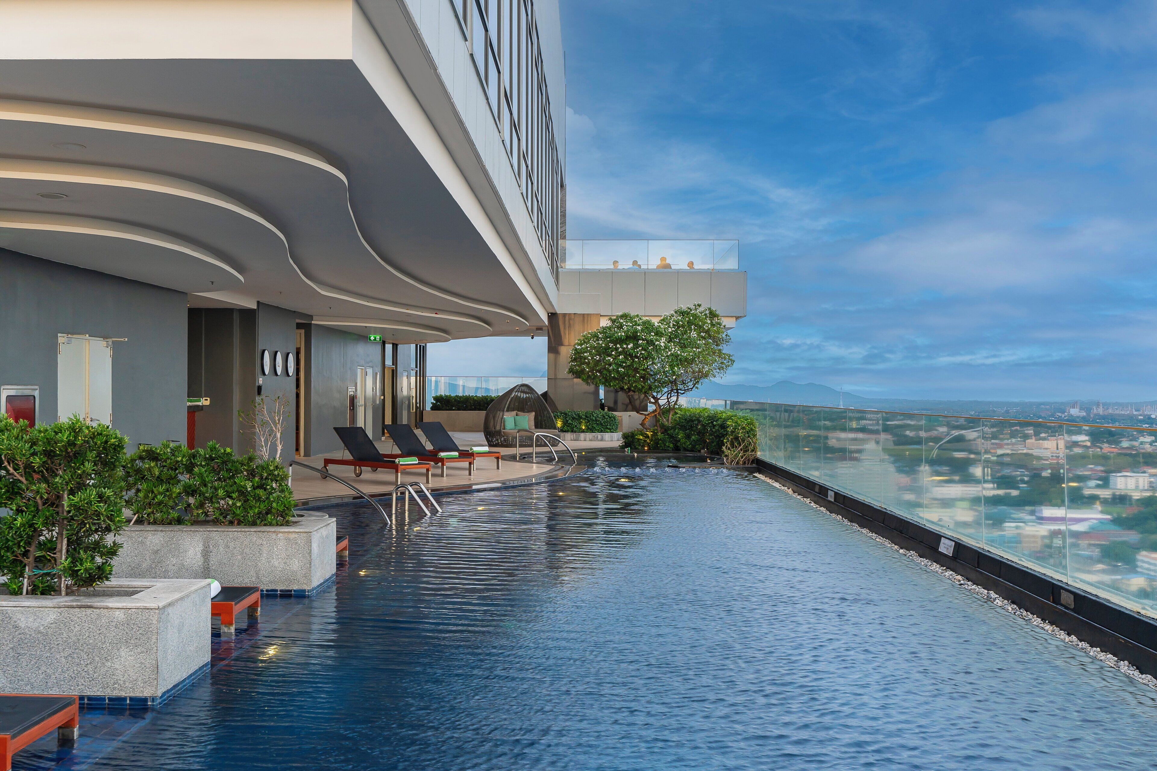 A rooftop infinity pool with lounge chairs and a view of the cityscape.