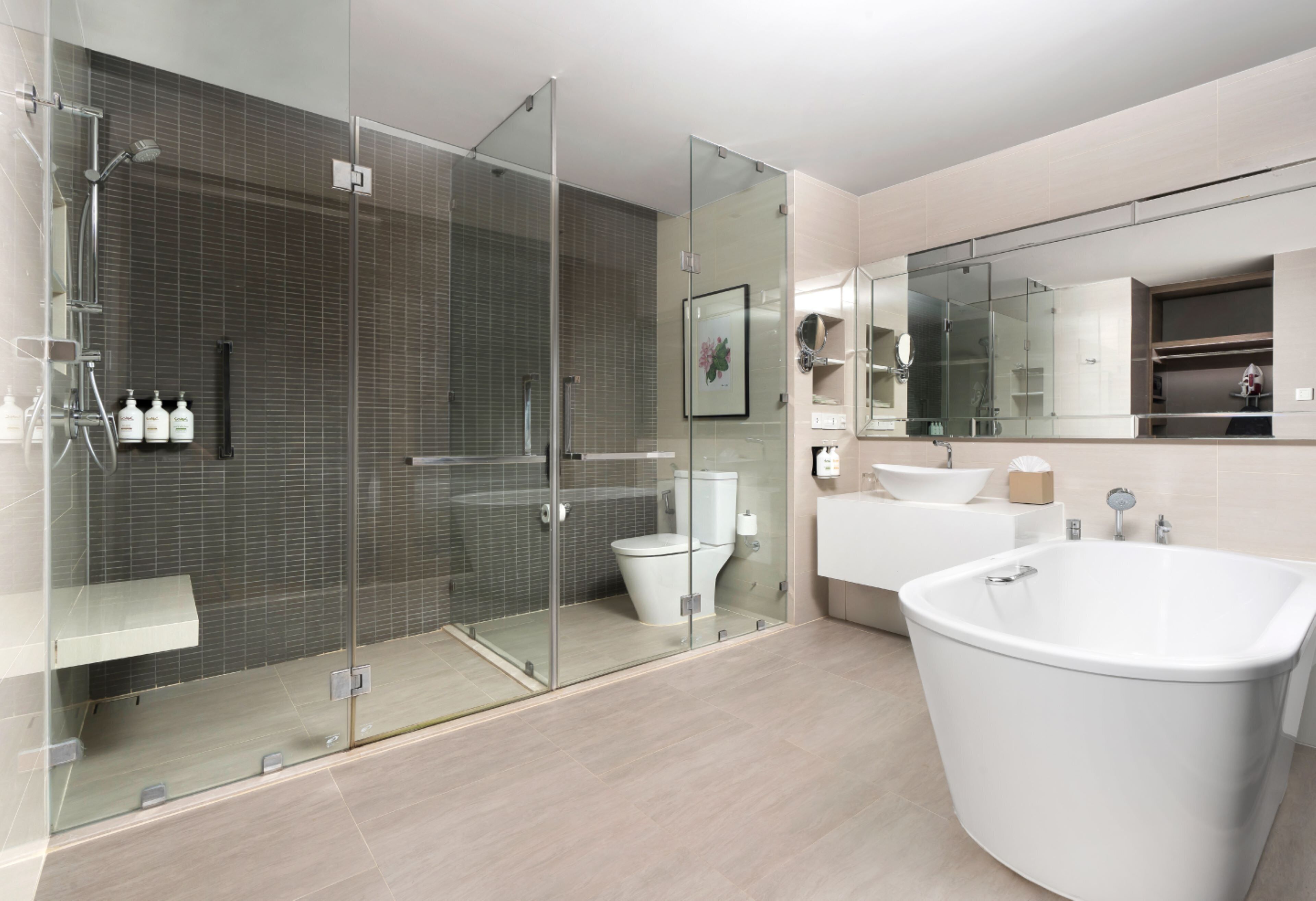 A modern bathroom with a glass-enclosed shower, a white toilet, a large bathtub, and a vanity with a mirror.