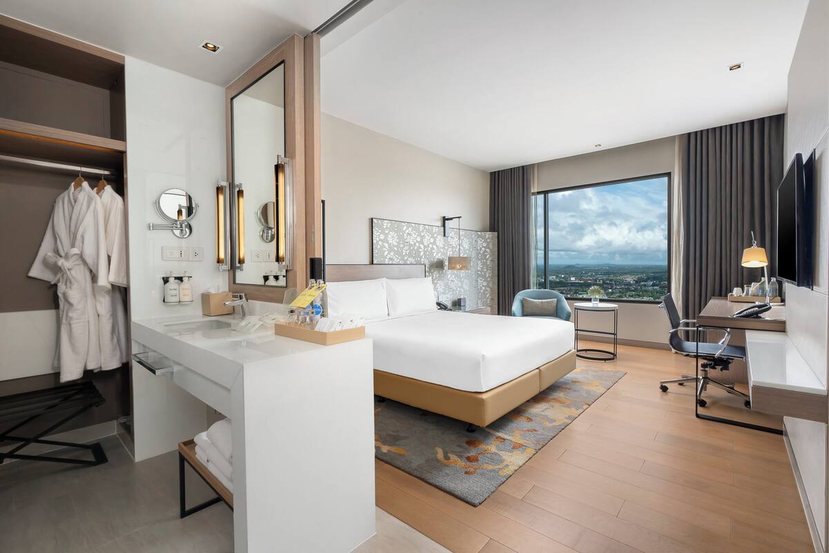A modern hotel room with a large bed, a desk, and a view of the city.