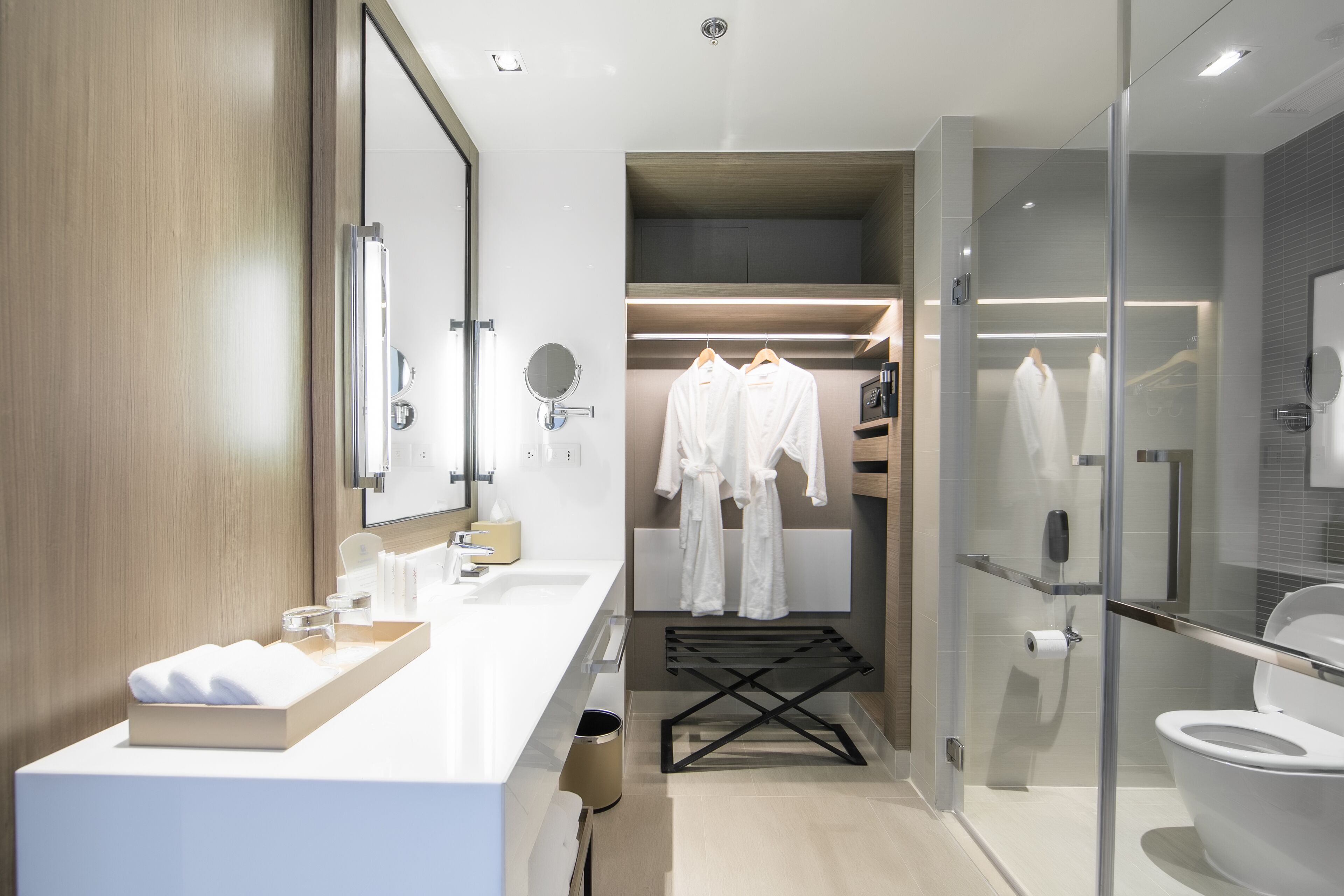 Een moderne badkamer met een douchecabine van glas, een wit wastafelmeubel met een beige aanrechtblad en een inloopkast met opbergplek voor gewaden.