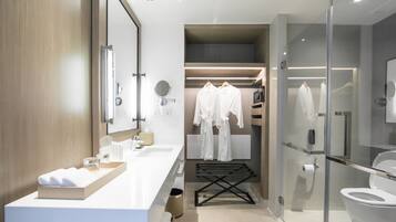 Een moderne badkamer met een douchecabine van glas, een wit wastafelmeubel met een beige aanrechtblad en een inloopkast met opbergplek voor gewaden.