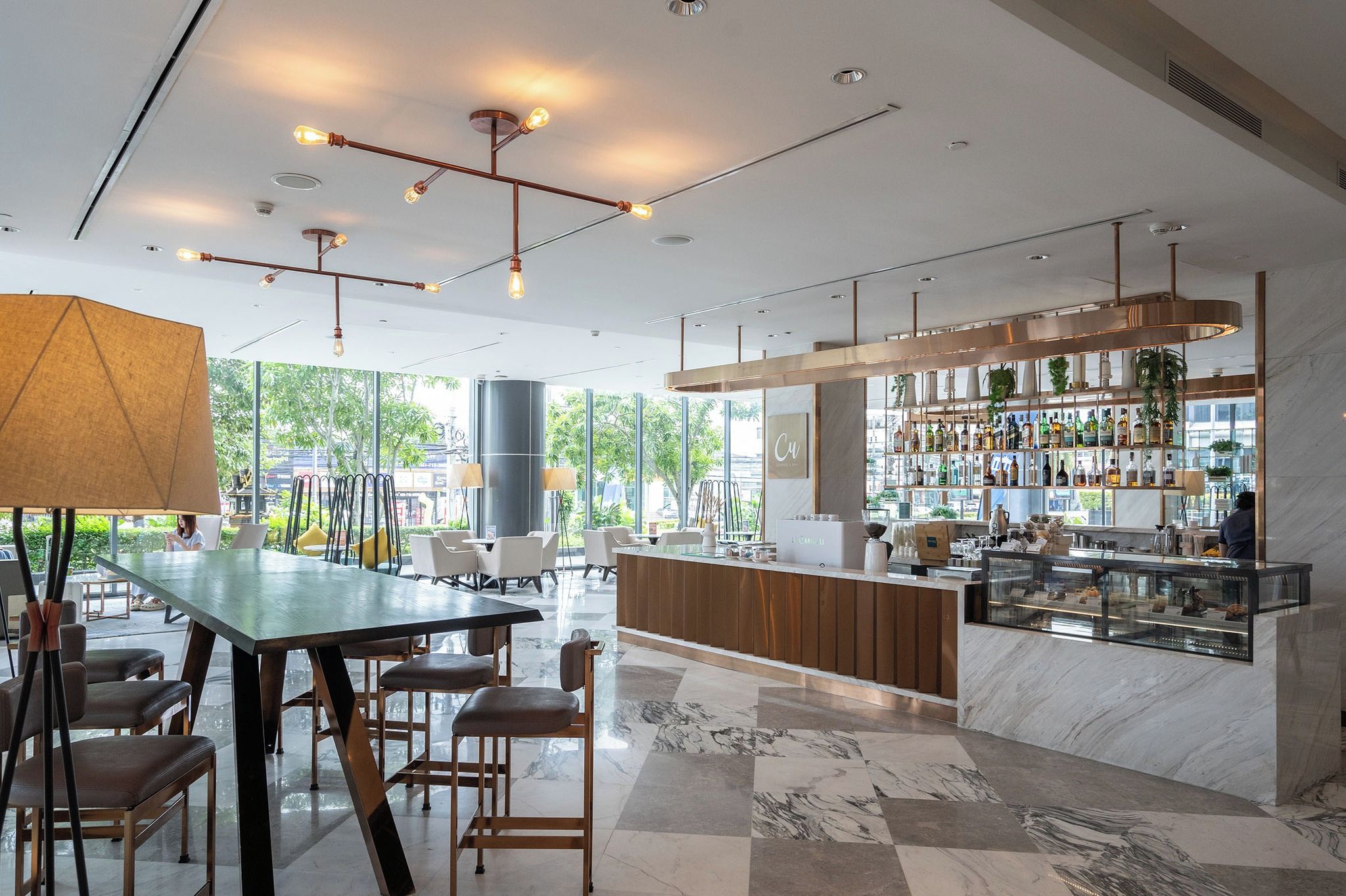 Un área de bar moderna con piso de mármol, una barra con vitrina de vidrio y vistas al exterior a través de amplios ventanales.
