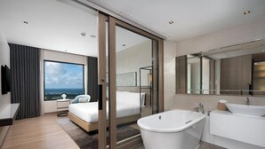 Una camera d'hotel moderna con un letto grande, bagno separato con vasca, un'ampia finestra vista città e televisione a schermo piatto.