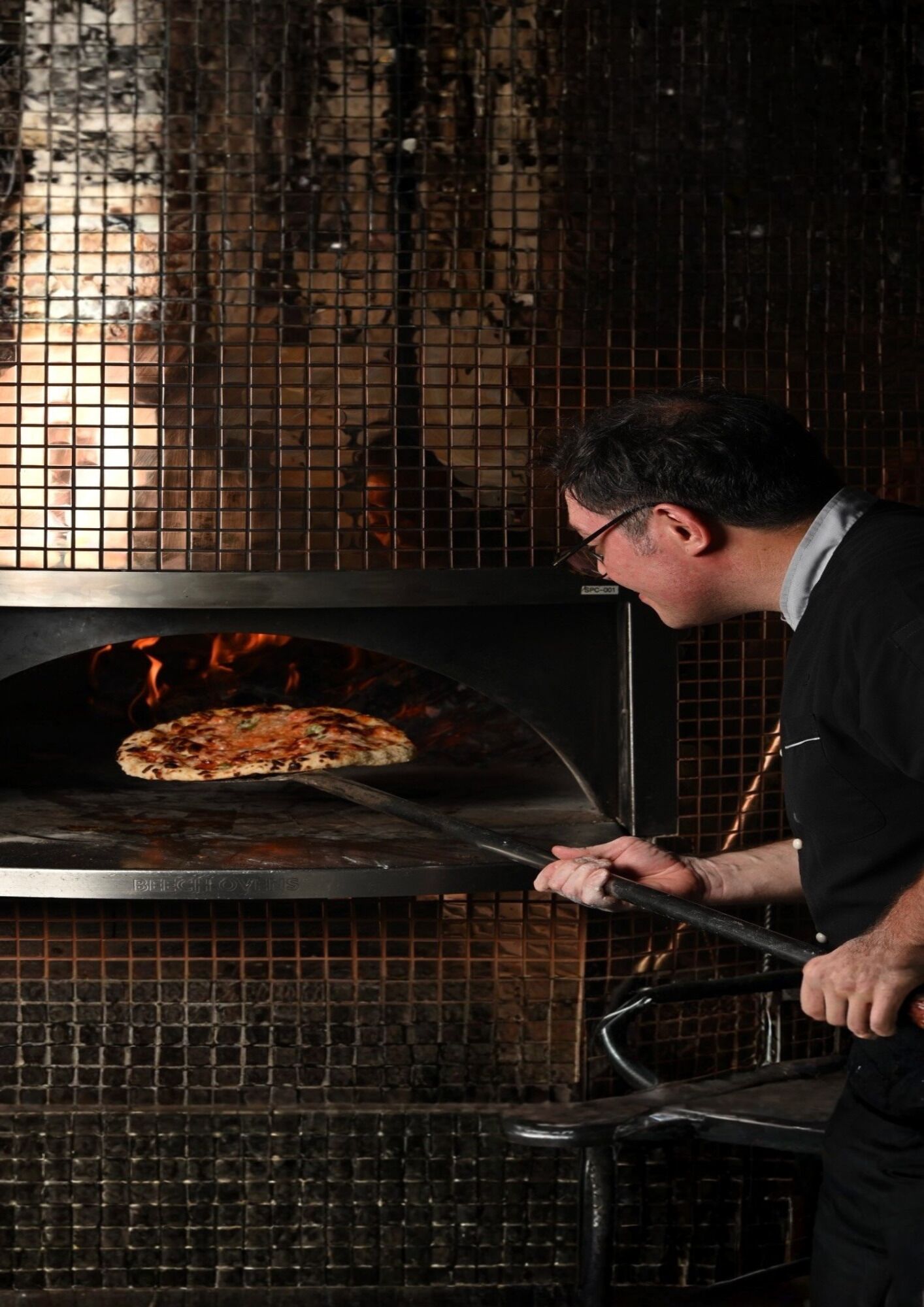 Una persona operando un horno de pizza de ladrillo.