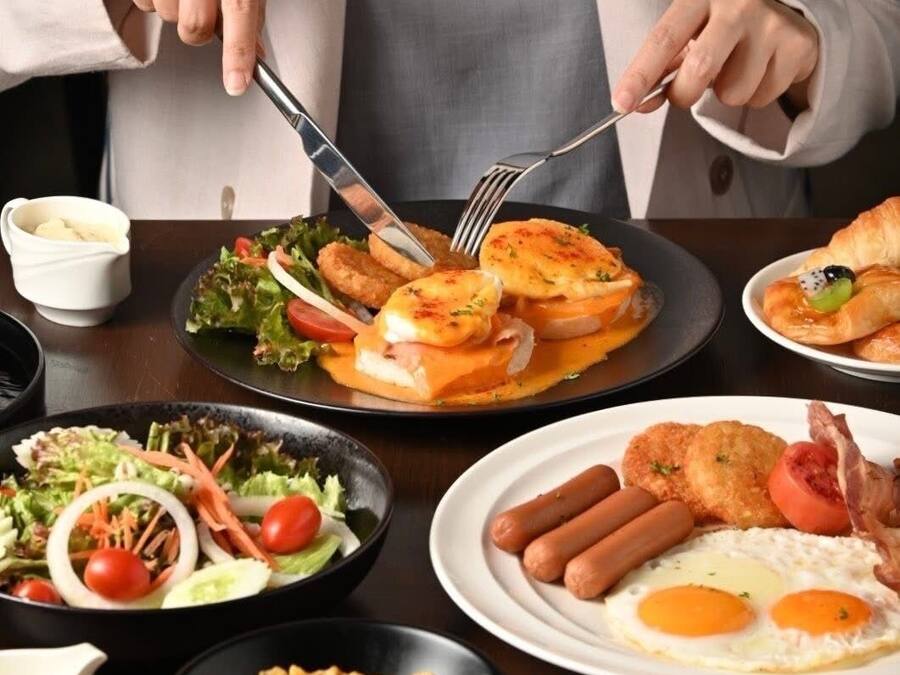 A person dining with a variety of dishes including eggs, sausages, and a salad.