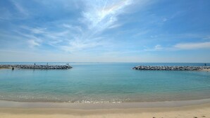 Una spiaggia con acque calme, cieli sereni e frangiflutti rocciosi.
