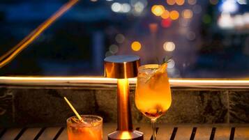 Une table dressée avec un cocktail, un verre d’une boisson claire, des brochettes de nourriture et un plat de mets frits.