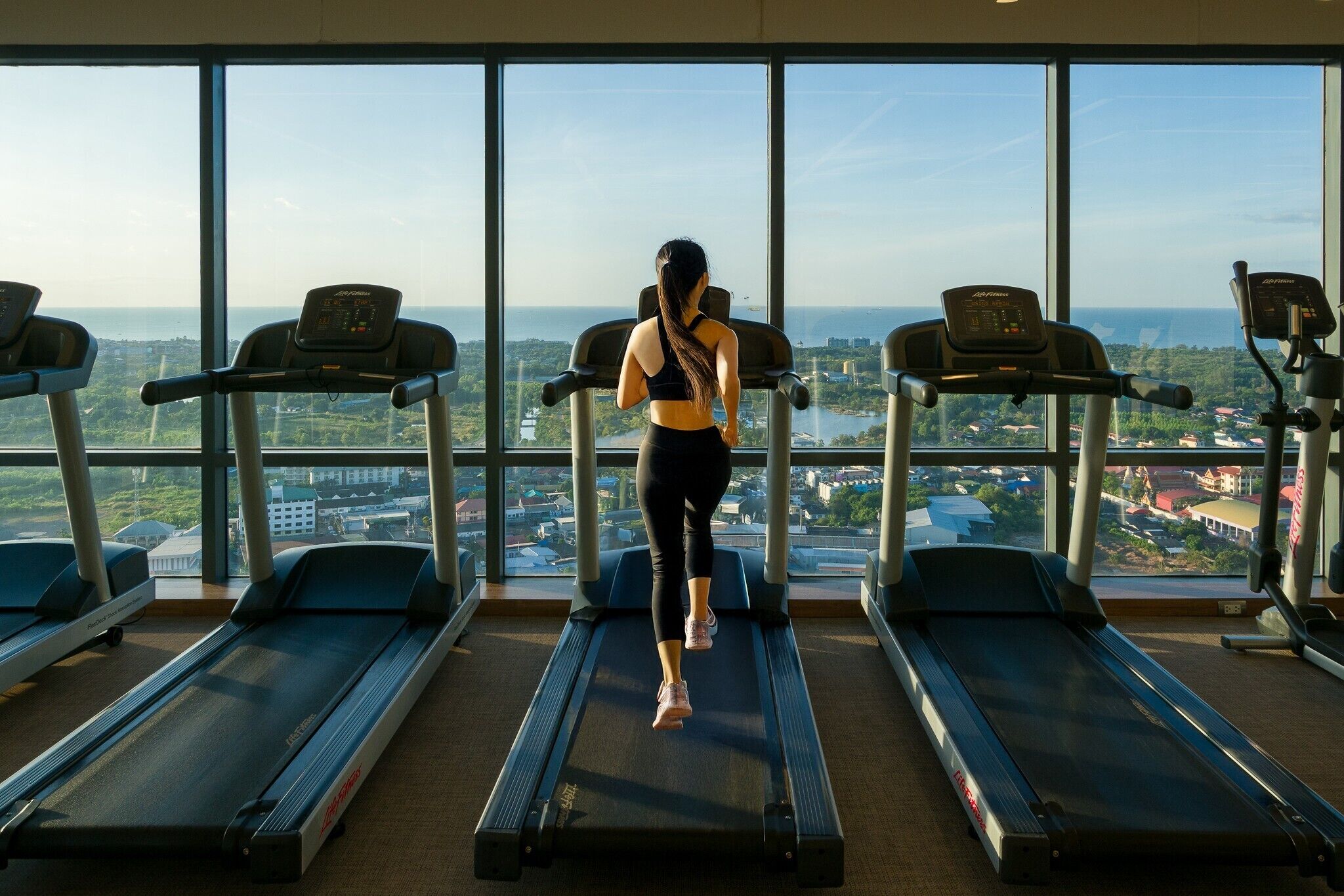 A gym with treadmills and a large window offering a city view.