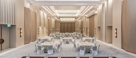 A large, well-lit conference room with round tables and chairs, equipped with water bottles and name cards.