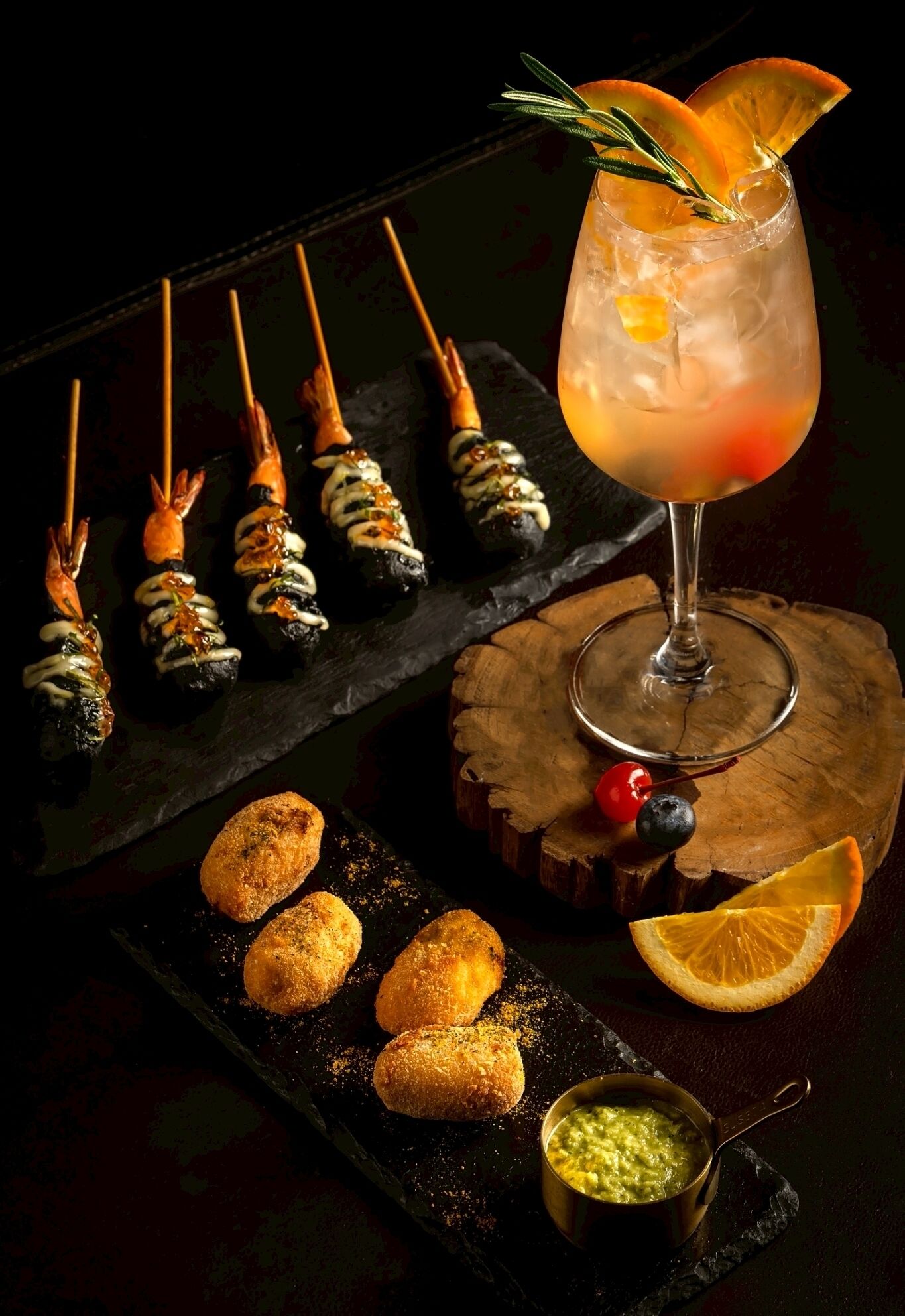 A dark setting with food items, a drink in a glass, and a wooden surface.