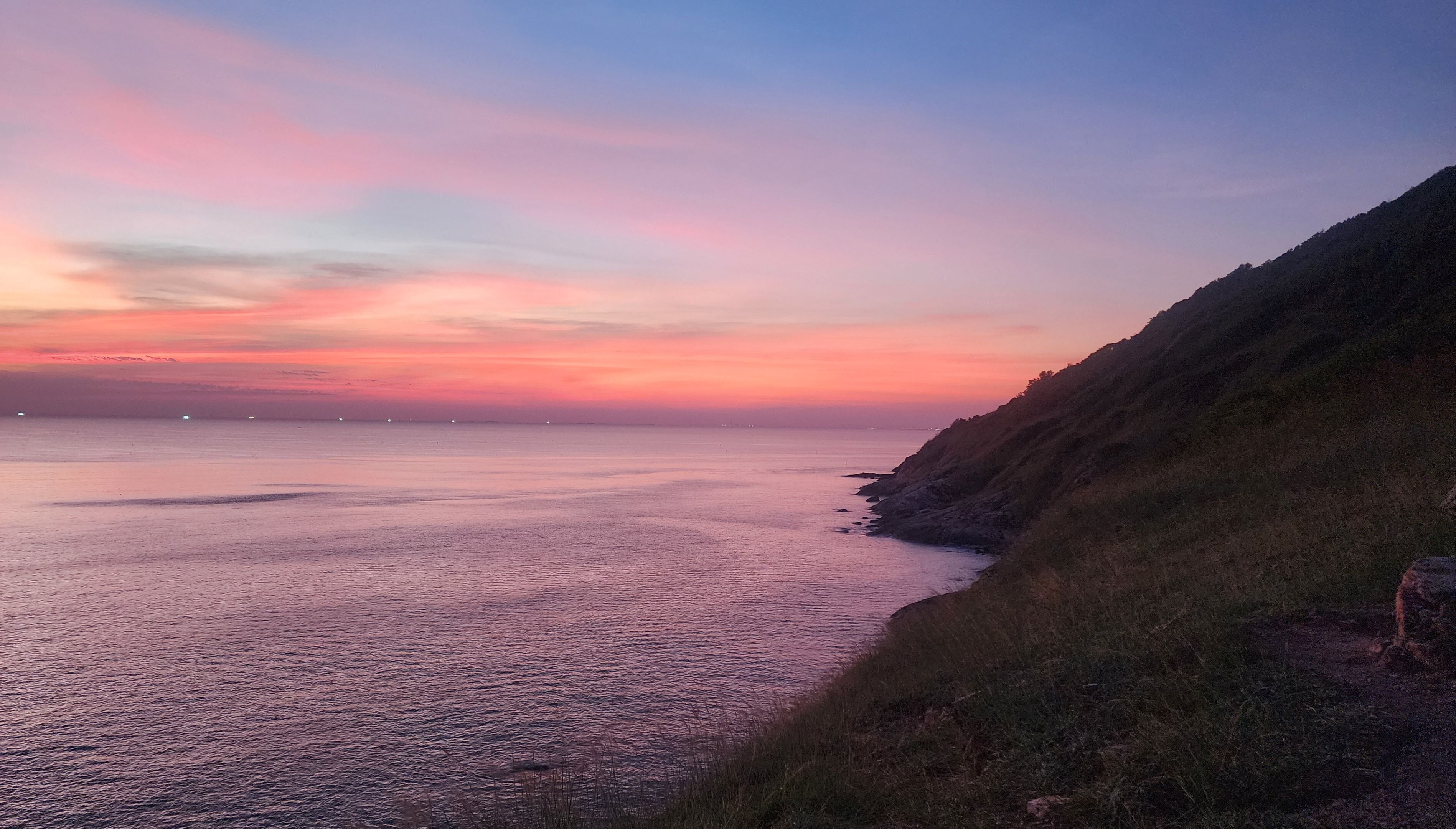 Paisagem costeira com mar calmo, um penhasco rochoso e céu ao pôr do sol.