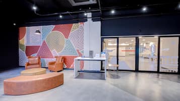 A modern office space with a colorful geometric wall mural, leather chairs, a round ottoman, and a glass door leading to another room.