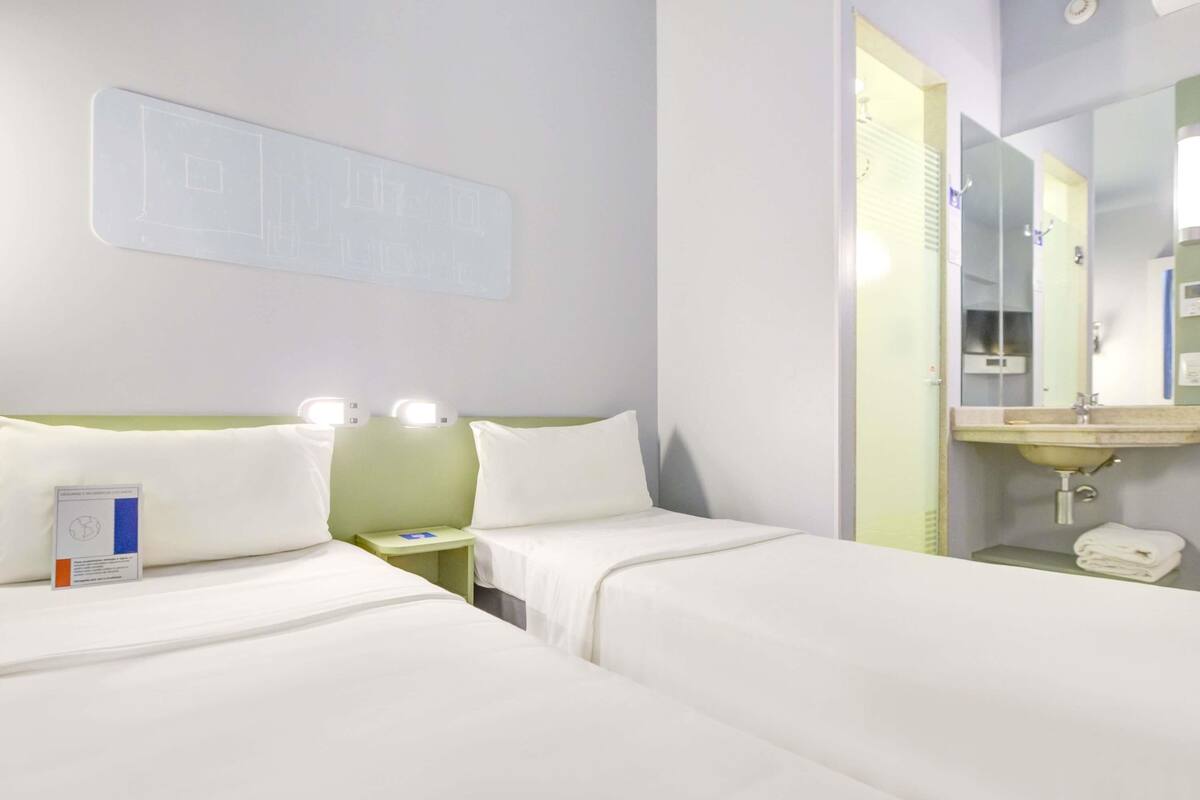 Une chambre d’hôtel avec deux lits, une table de chevet, un miroir et un lavabo.