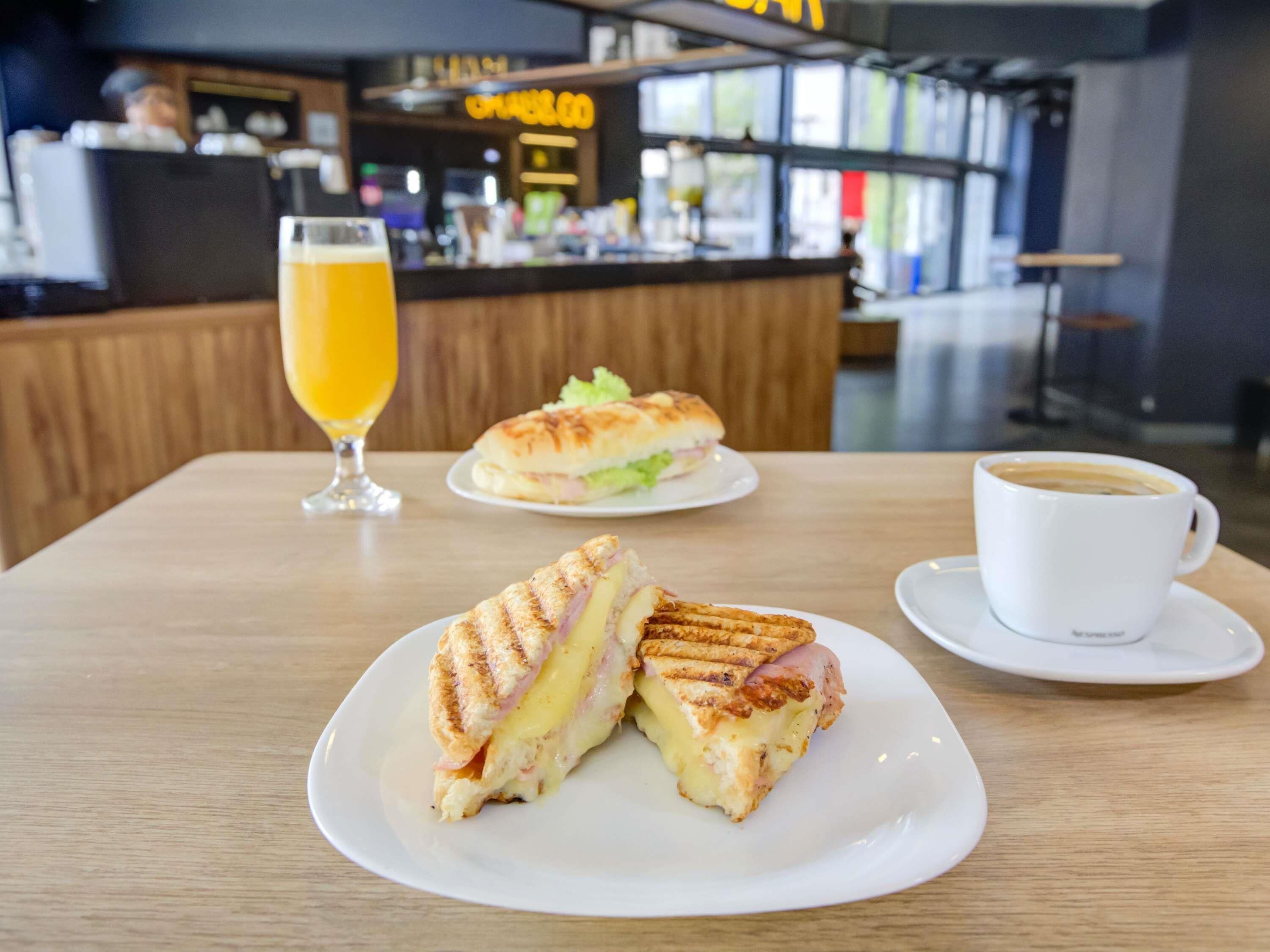 A sandwich on a plate, a glass of orange juice, and a cup of coffee on a table in a cafe.