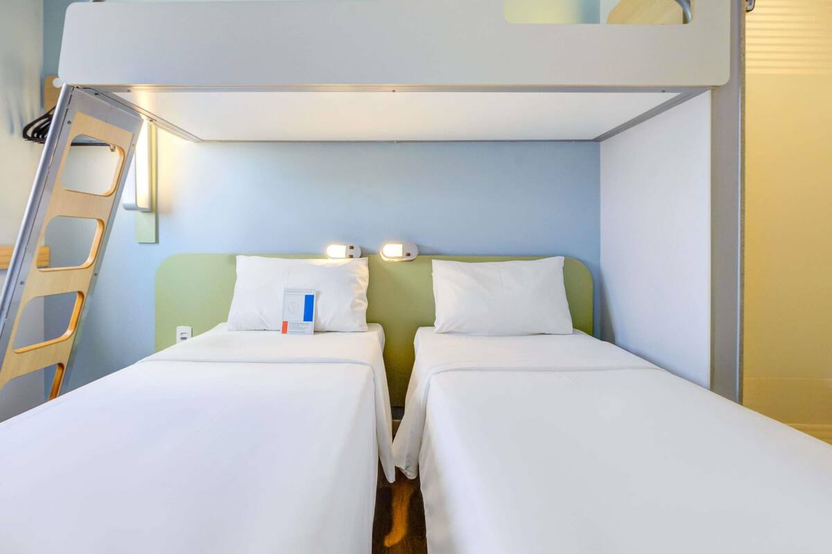 Une chambre avec un lit superposé, comprenant deux lits, une échelle et un luminaire fixé au mur.