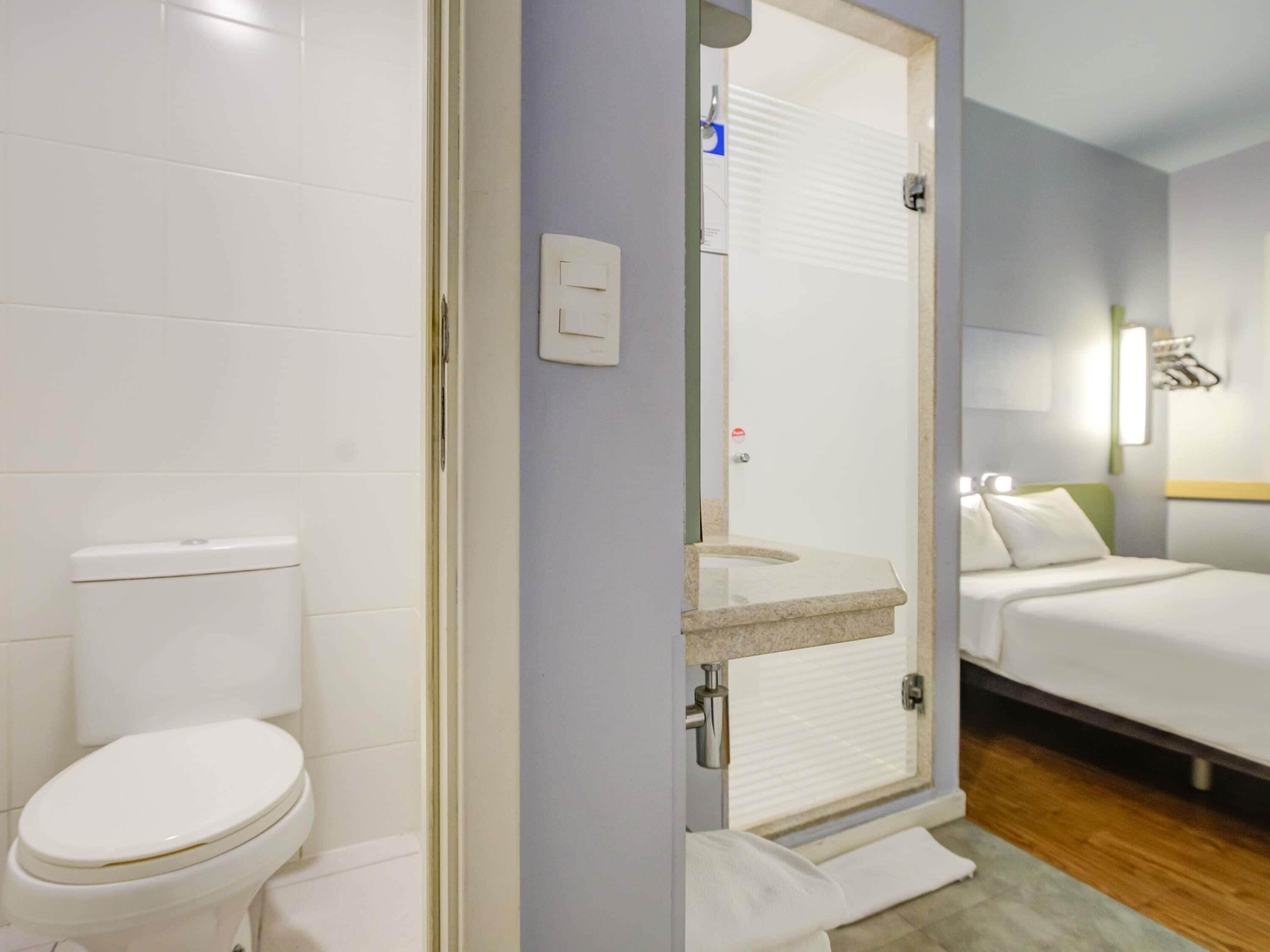 Un baño con inodoro, zona de ducha y cama con cabecera.