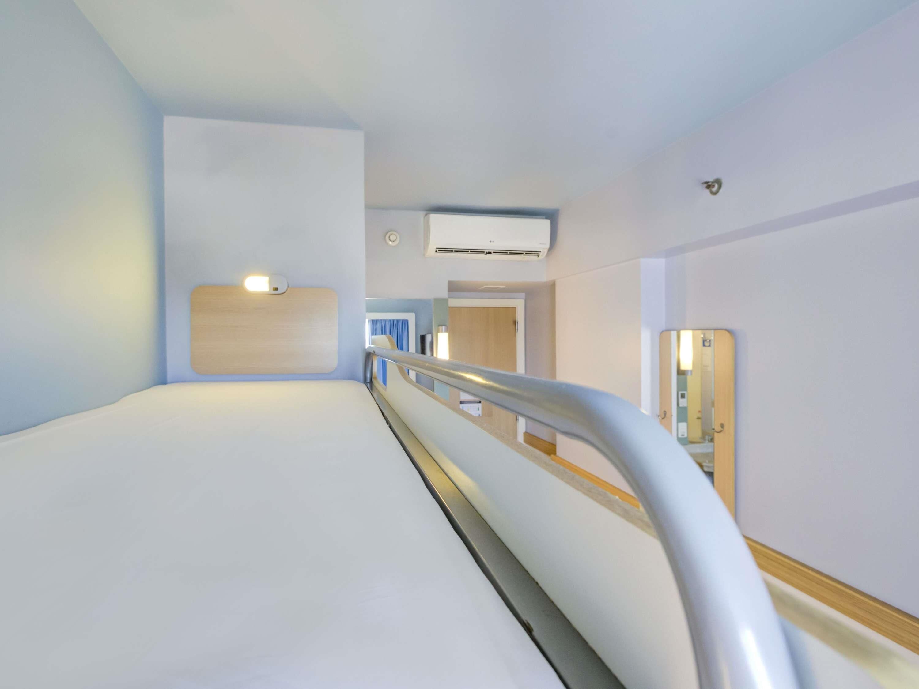 Un pasillo moderno de hotel con una cama, un pasamanos, un espejo y un equipo de aire acondicionado.
