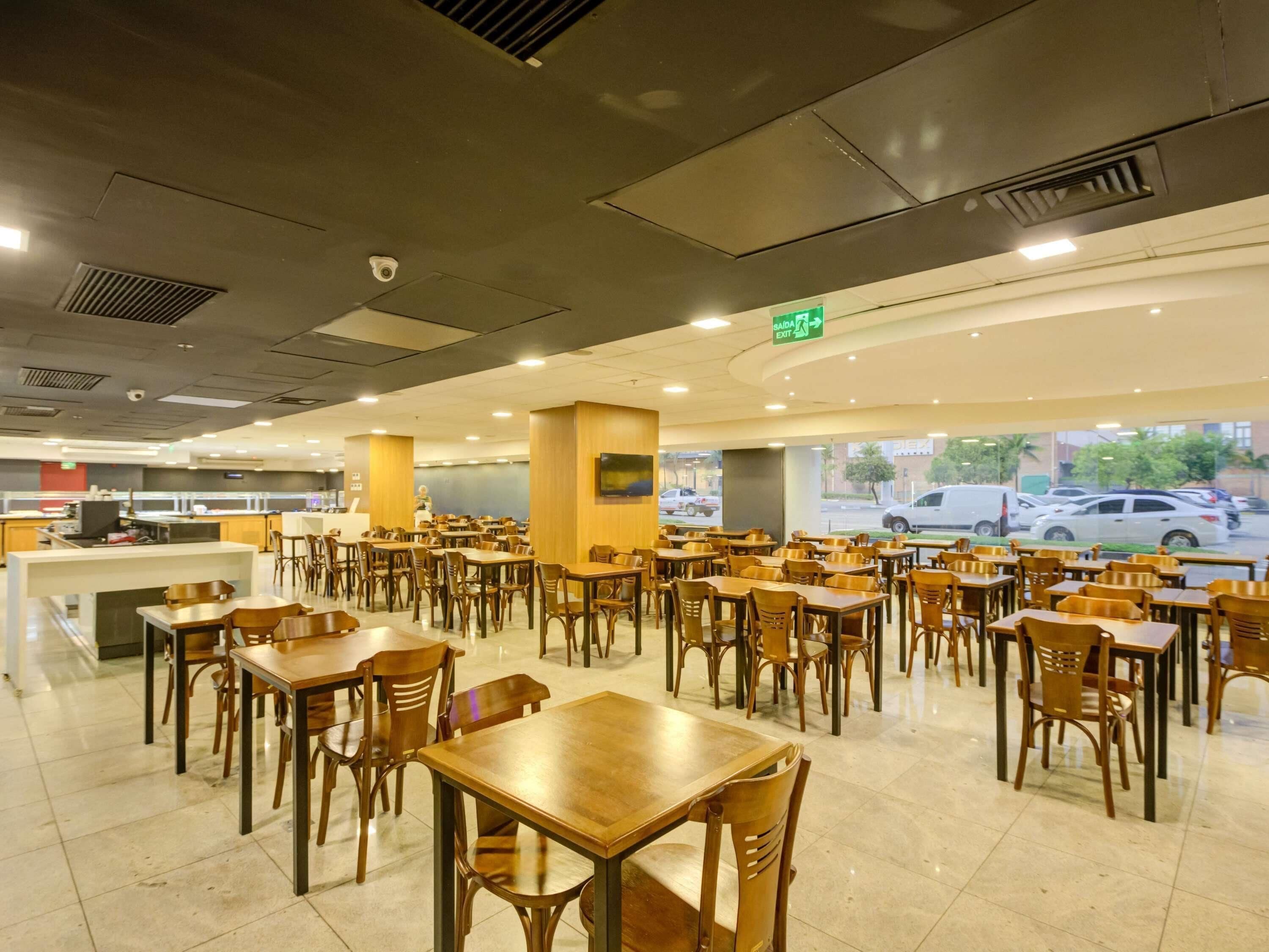 A spacious indoor dining area with multiple wooden tables and chairs, a counter with a cash register, and a view of parked cars outside.
