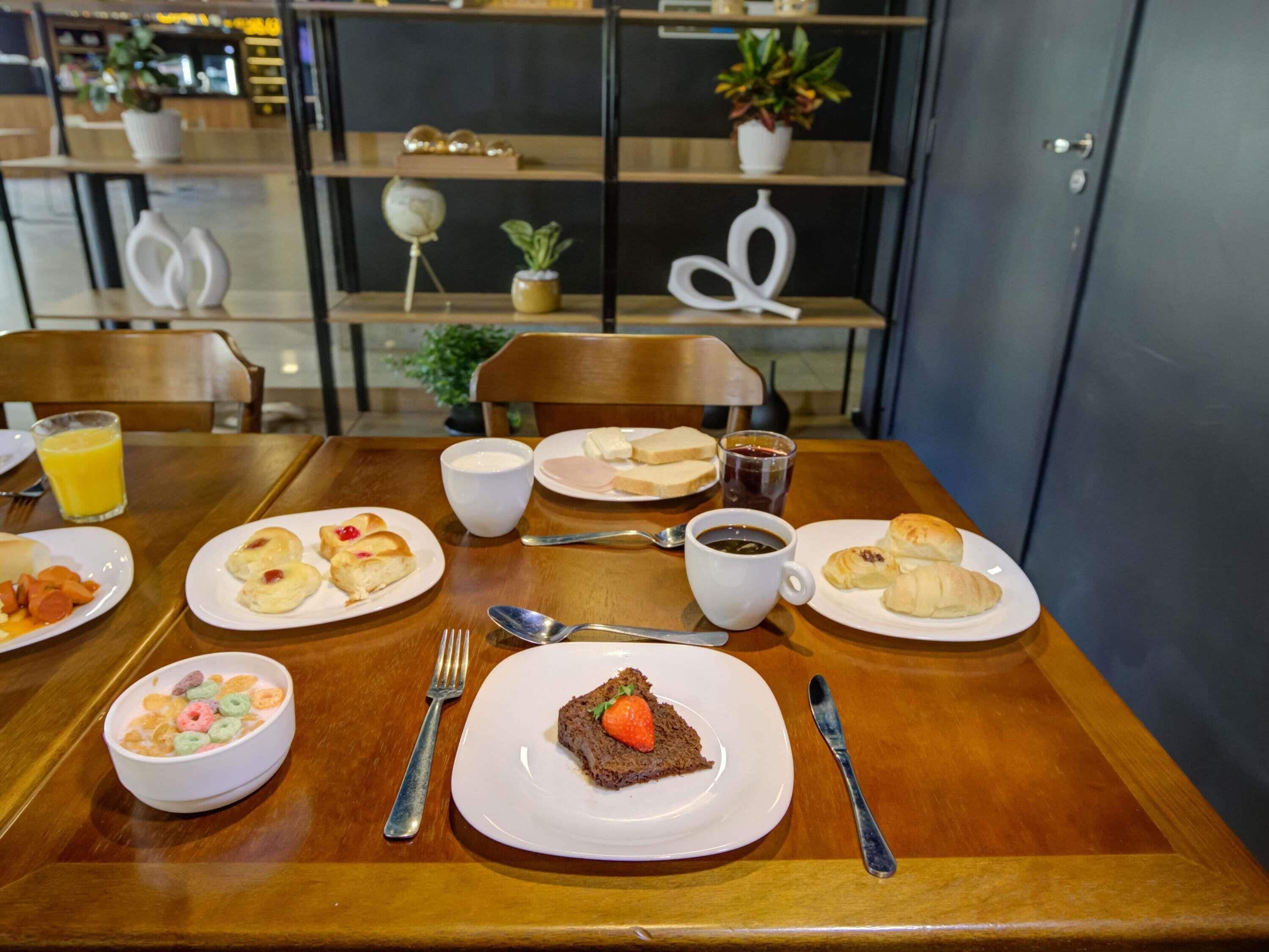 A dining table with breakfast items including cereal, pastries, and a slice of cake.