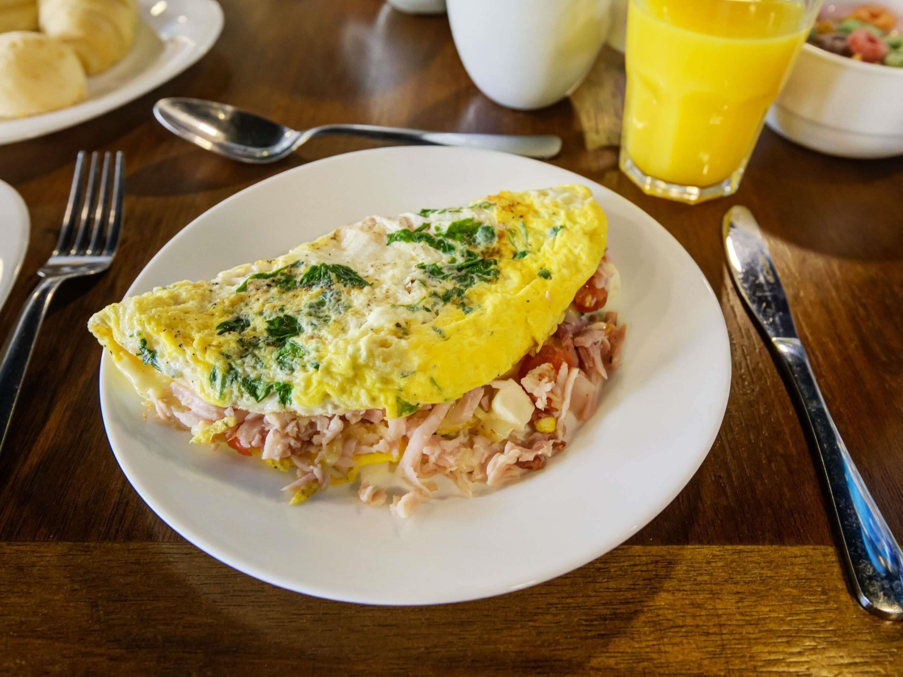 A plate of food with an omelette on a white plate, accompanied by a glass of orange juice and a bowl of salad.