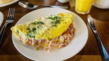 A plate of food with an omelette on a white plate, accompanied by a glass of orange juice and a bowl of salad.