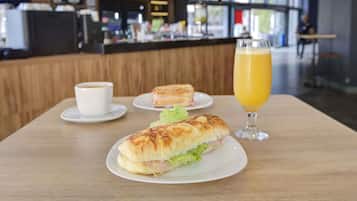 A restaurant setting with a sandwich, a glass of orange juice, and a cup of coffee on a table.