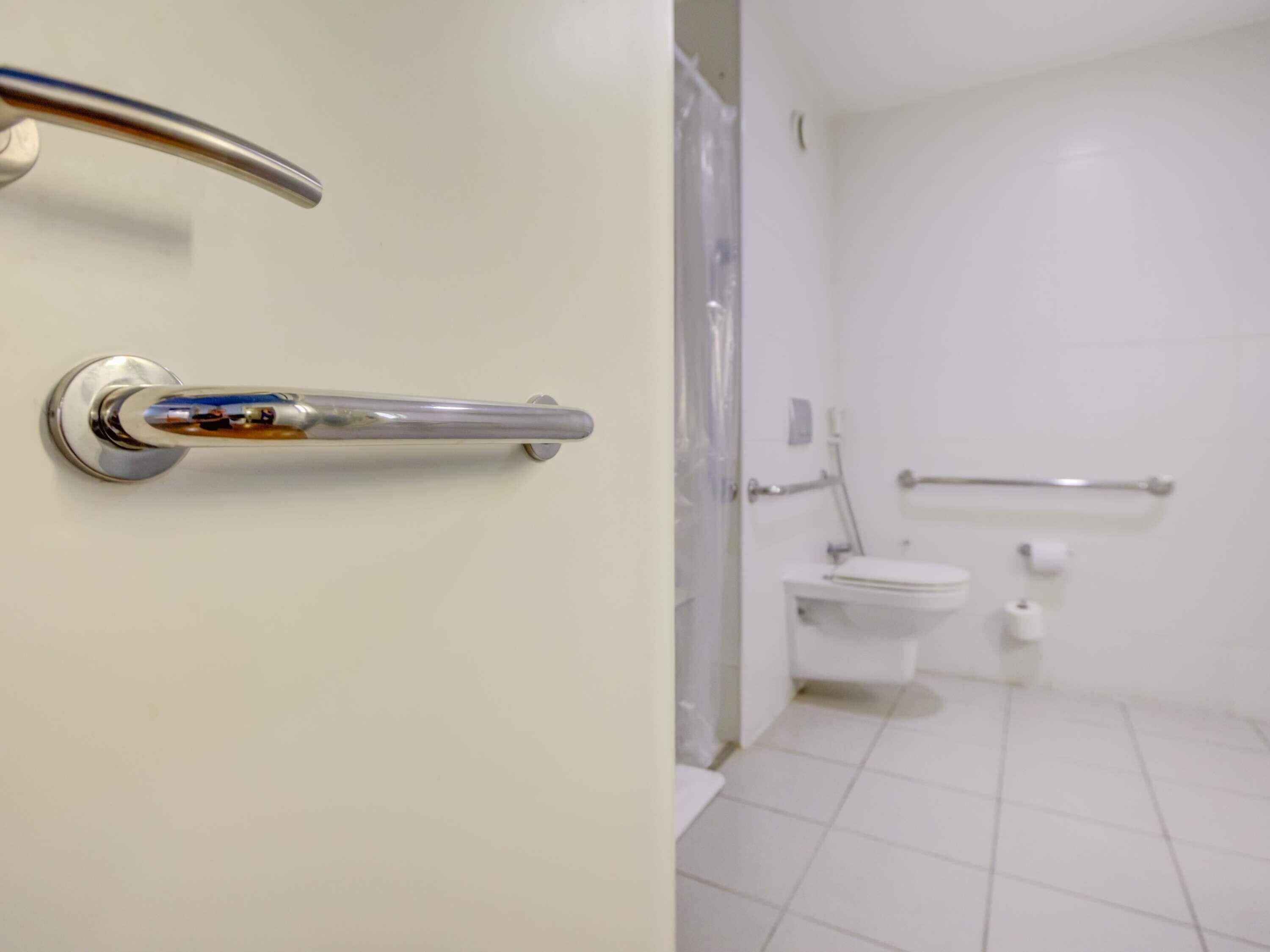 Un bagno con il water bianco, un corrimano e una zona doccia.