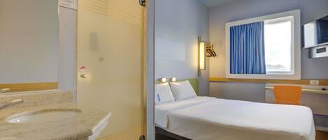 A hotel room with a bed, a bedside table, a TV, and a window with curtains.