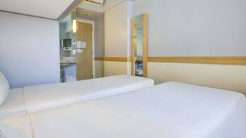 A hotel room with two single beds, a large mirror, and a bathroom visible through an open door.