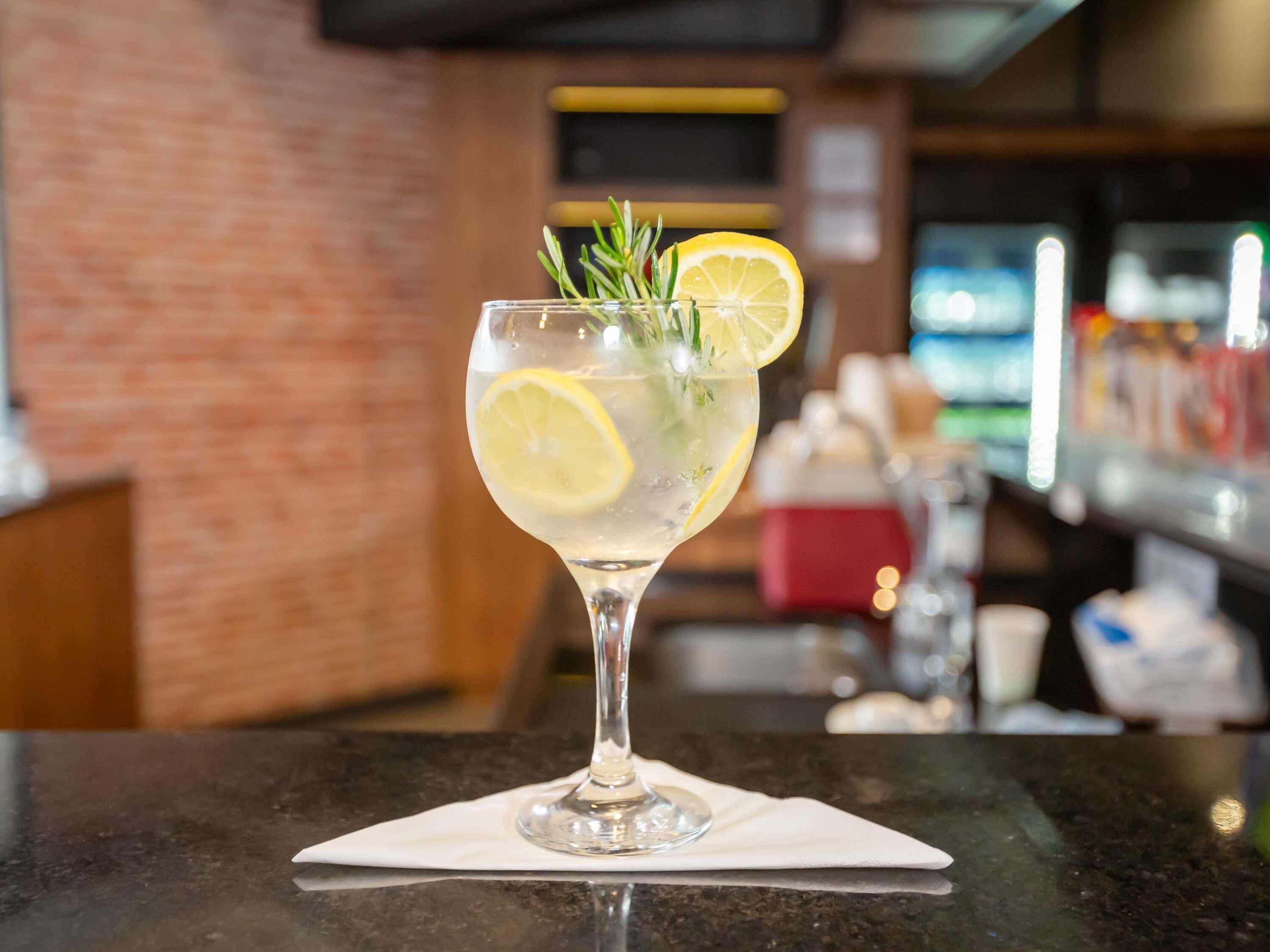 Un verre à cocktail, orné d’une tranche de citron et d’une branche de romarin, posé sur le comptoir d’un bar.