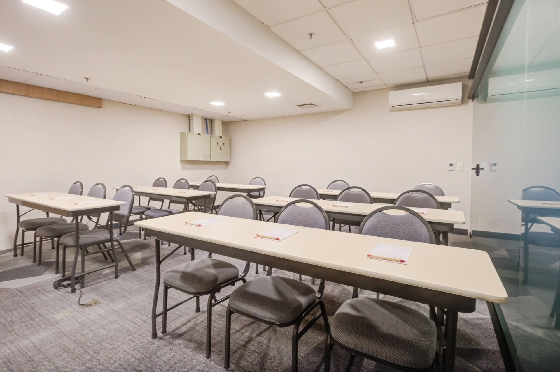 A conference room with multiple tables and chairs, a whiteboard, and an air conditioning unit on the wall.