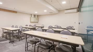 A conference room with multiple tables and chairs, a whiteboard, and an air conditioning unit on the wall.