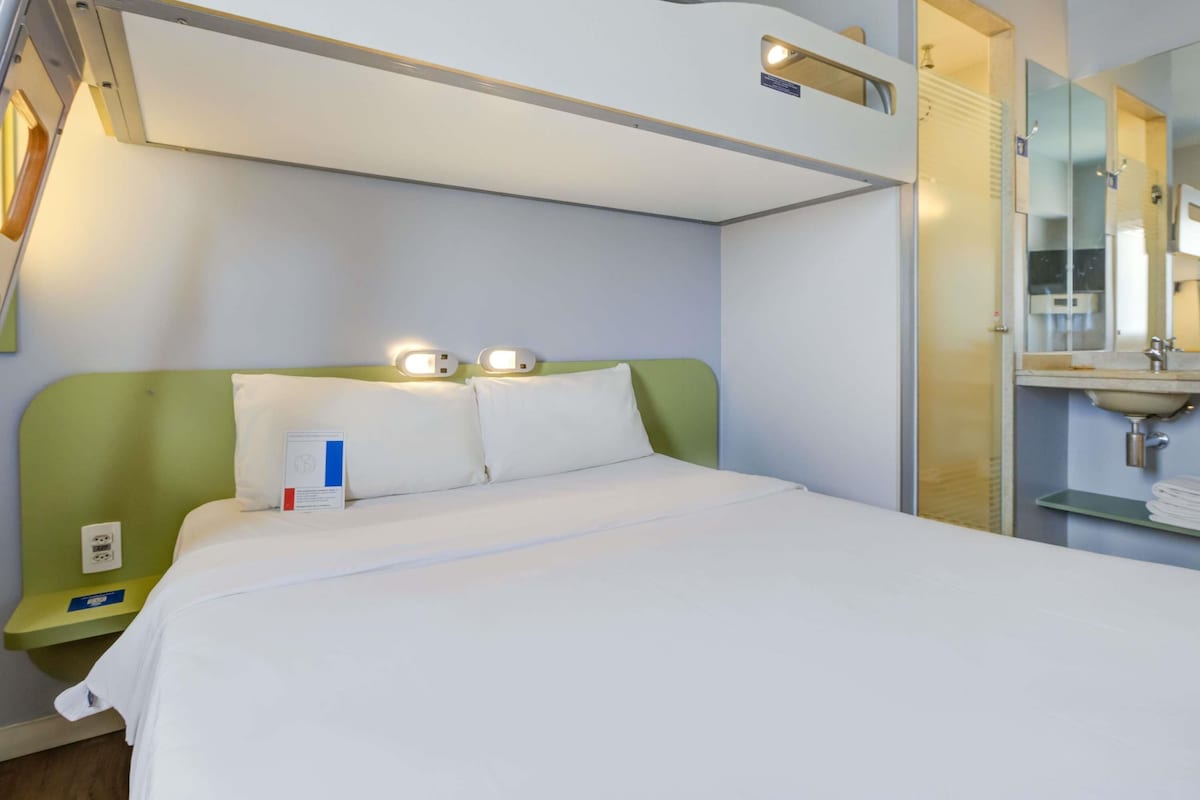 A hotel room with a bed, bedside table, and a bathroom with a sink and mirror.