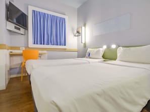 A hotel room with two beds, a desk, a chair, a TV, and a window with curtains.