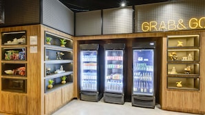 Winkelinterieur met houten planken, een neonbord waarop 'GRAB & GO' staat en gekoelde vitrines.