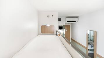 A narrow corridor with a bed, a wooden panel, a handrail, and a mirror on the wall.