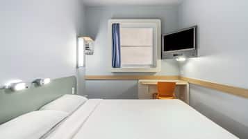 Habitación de hotel con cama, escritorio, silla, televisor y ventana con cortinas.