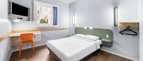 Una camera da letto con un letto, una scrivania, una sedia, una TV e una finestra con tende.
