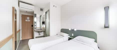 Habitación de hotel con dos camas, un baño con espejo y un pasillo que conduce a otra habitación.