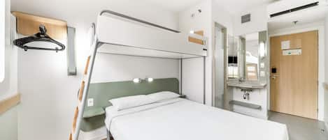 A bunk bed room with a wooden floor, a small bedside table, a mirror, and a wooden door.