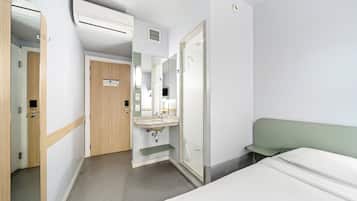 A hotel room with a bed, a sink, a mirror, and a door.