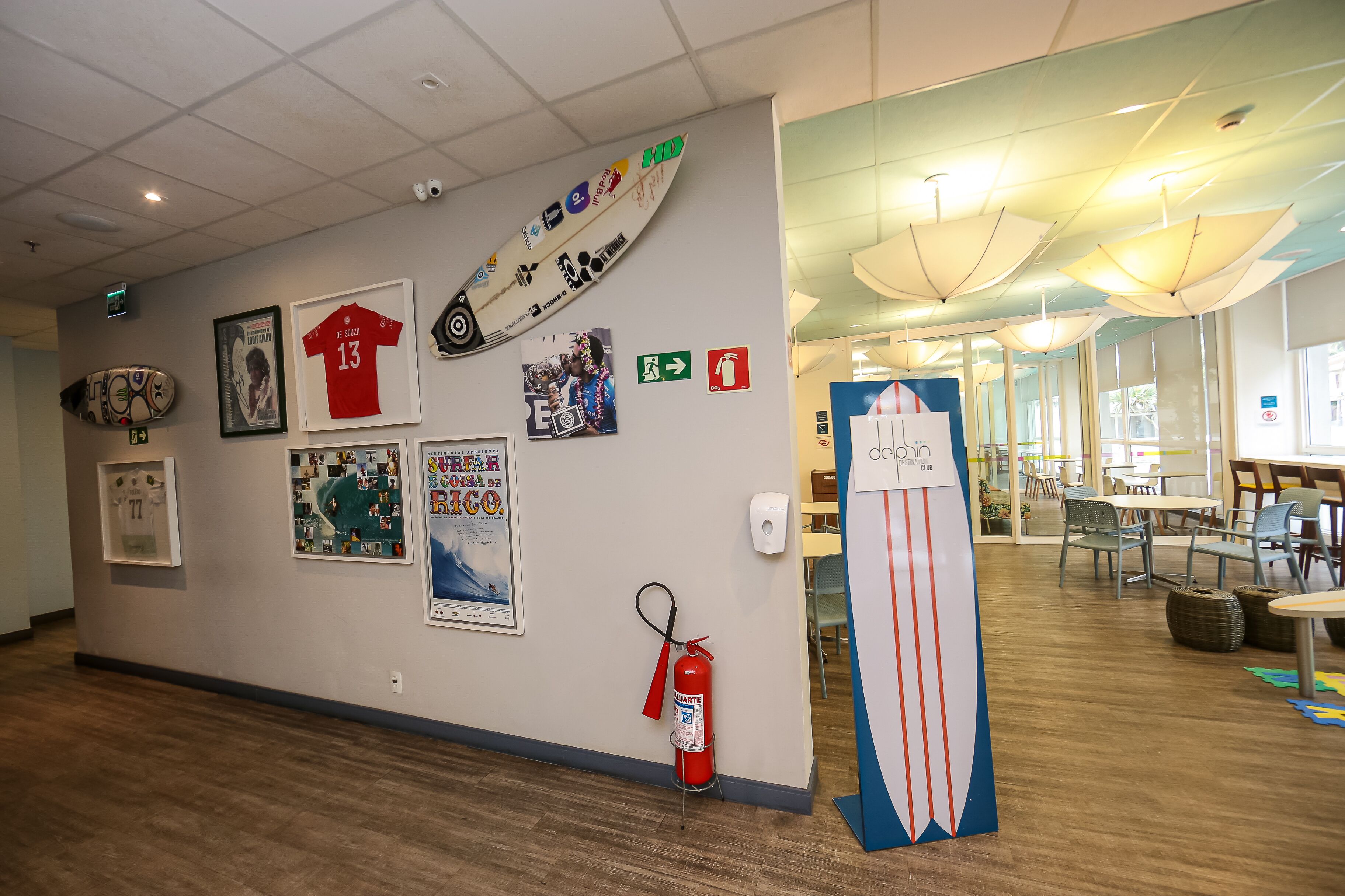 Un pasillo con extintor, una tabla de surf y varios carteles en la pared.