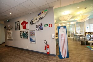 Un pasillo con extintor, una tabla de surf y varios carteles en la pared.