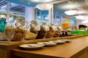 A breakfast buffet with various food items in glass containers, plates, and cutlery on a wooden counter. - Golden Tulip Guarujá (Guarujá)