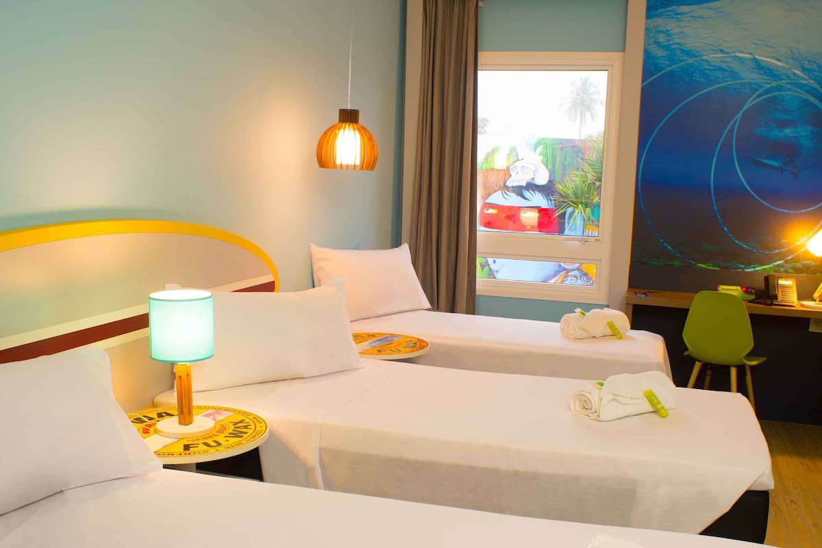 A hotel room with two beds, a desk, a lamp, and a large window with a view of palm trees.