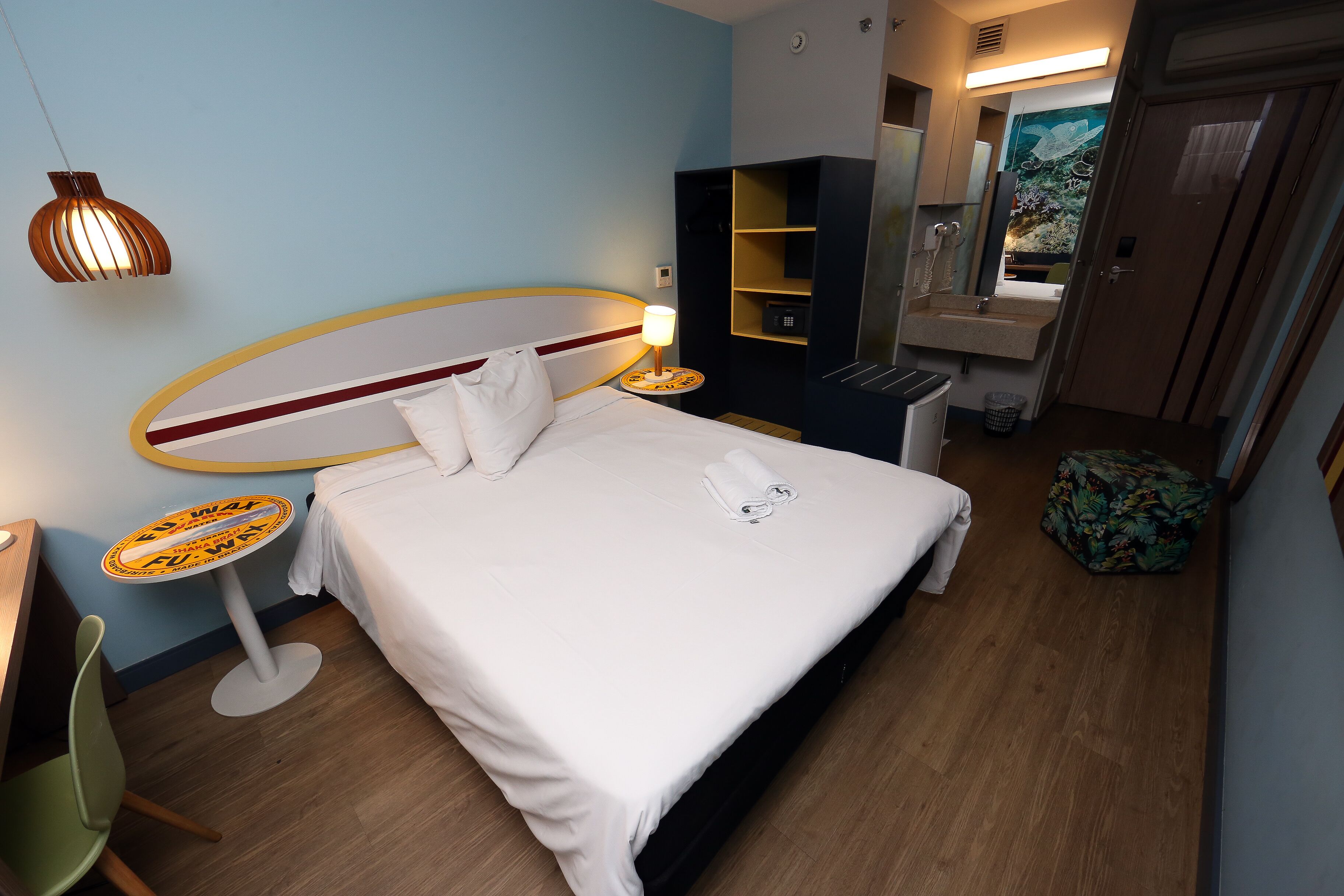 A hotel room with a bed, a small round table with a lamp, a chair, a sink, and a mirror.