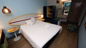 A hotel room with a bed, a small round table with a lamp, a chair, a sink, and a mirror.