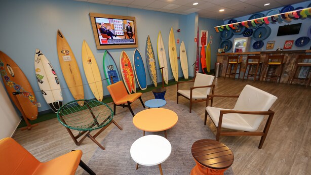 A room with surfboards against the wall, a television, and a bar area with chairs and tables. - Golden Tulip Guarujá (Former Delphin Surf Hotel) (Guarujá)