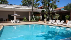 A swimming pool with lounge chairs and a covered seating area. - Golden Tulip Guarujá (Former Delphin Surf Hotel) (Guarujá)