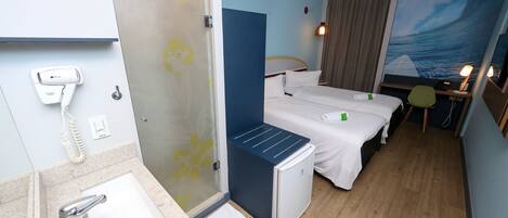 A hotel room with a shower, a sink, a bed, a desk, and a painting of a wave.